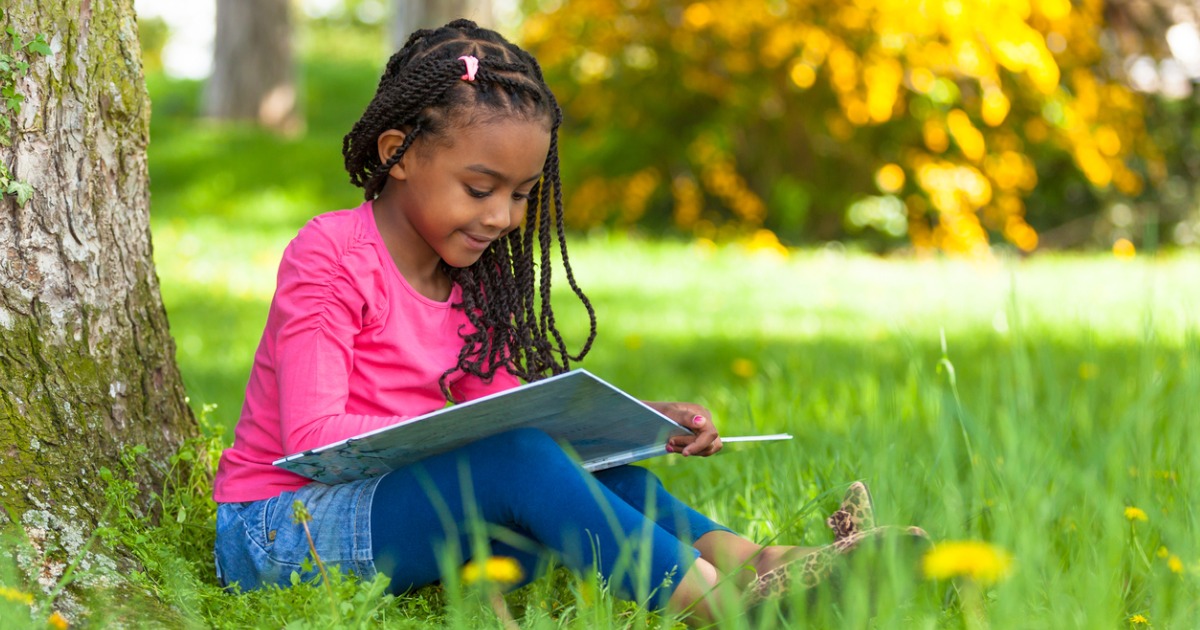 A young girl sits outside and reads a book