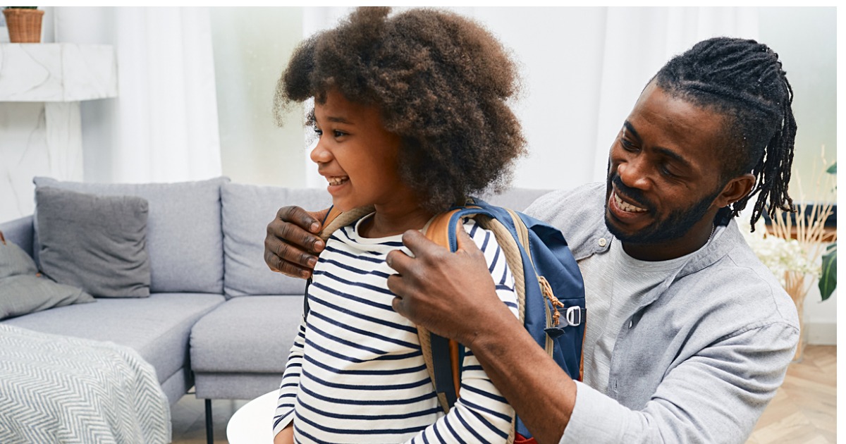 A dad helps his child put their backpack on