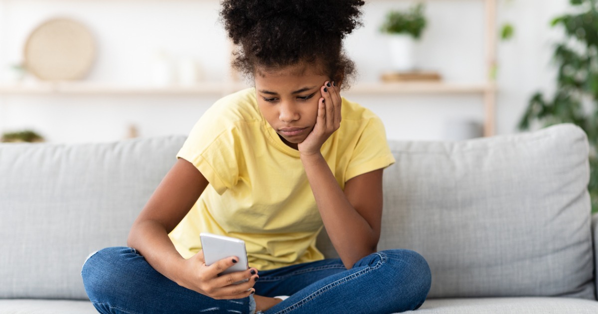 A young girl sits and looks sadly at her phone