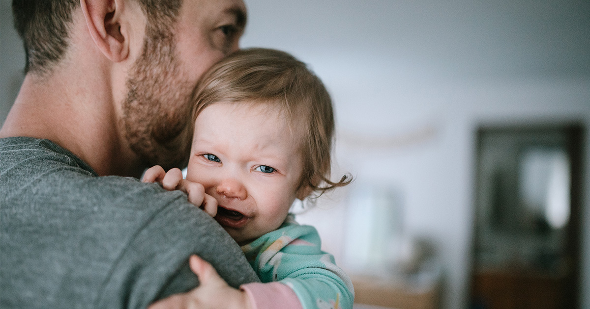 A dad holds his crying toddler