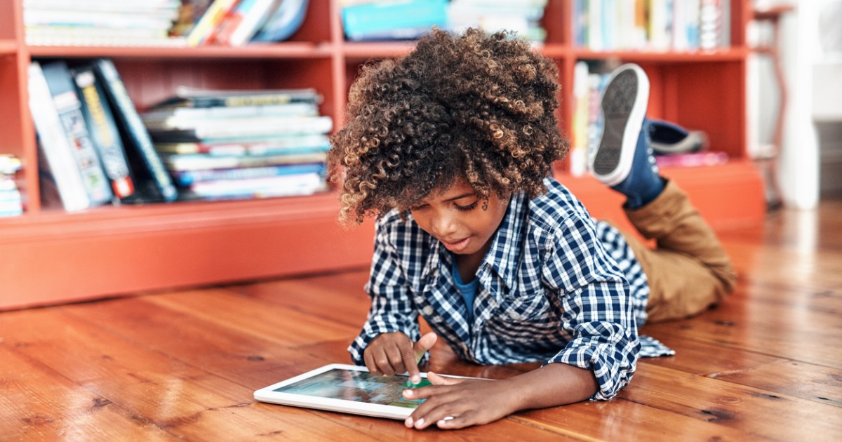 Young boy lies on the ground and plays with a tablet