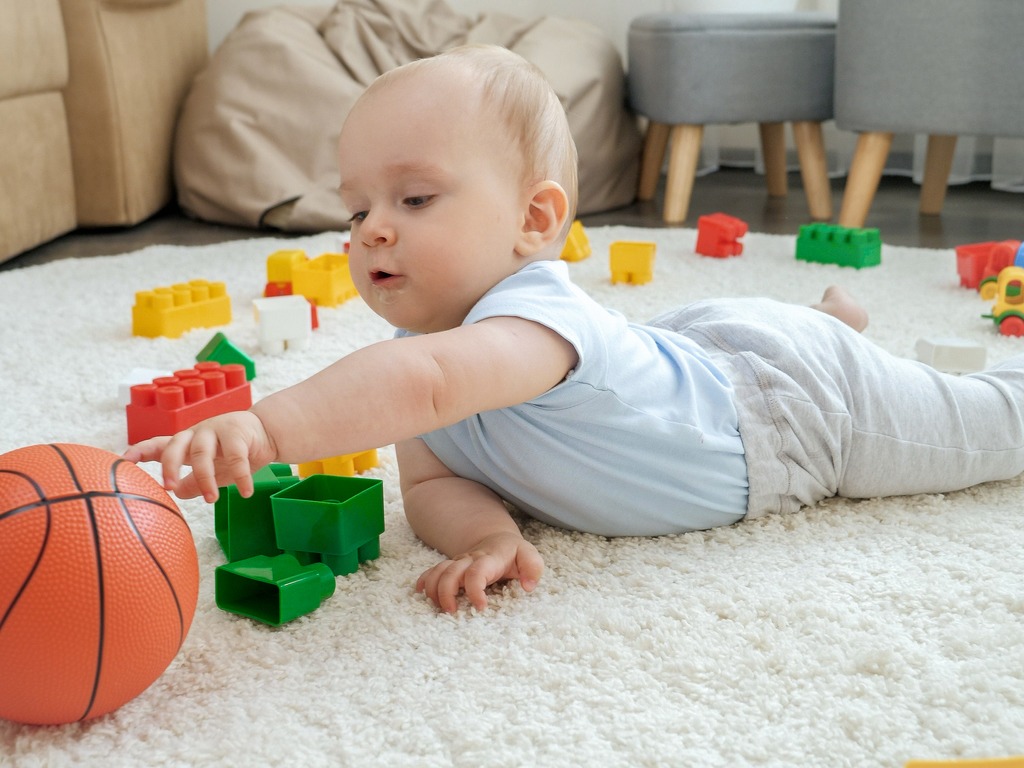 Cute baby boy playing with toys on carpet