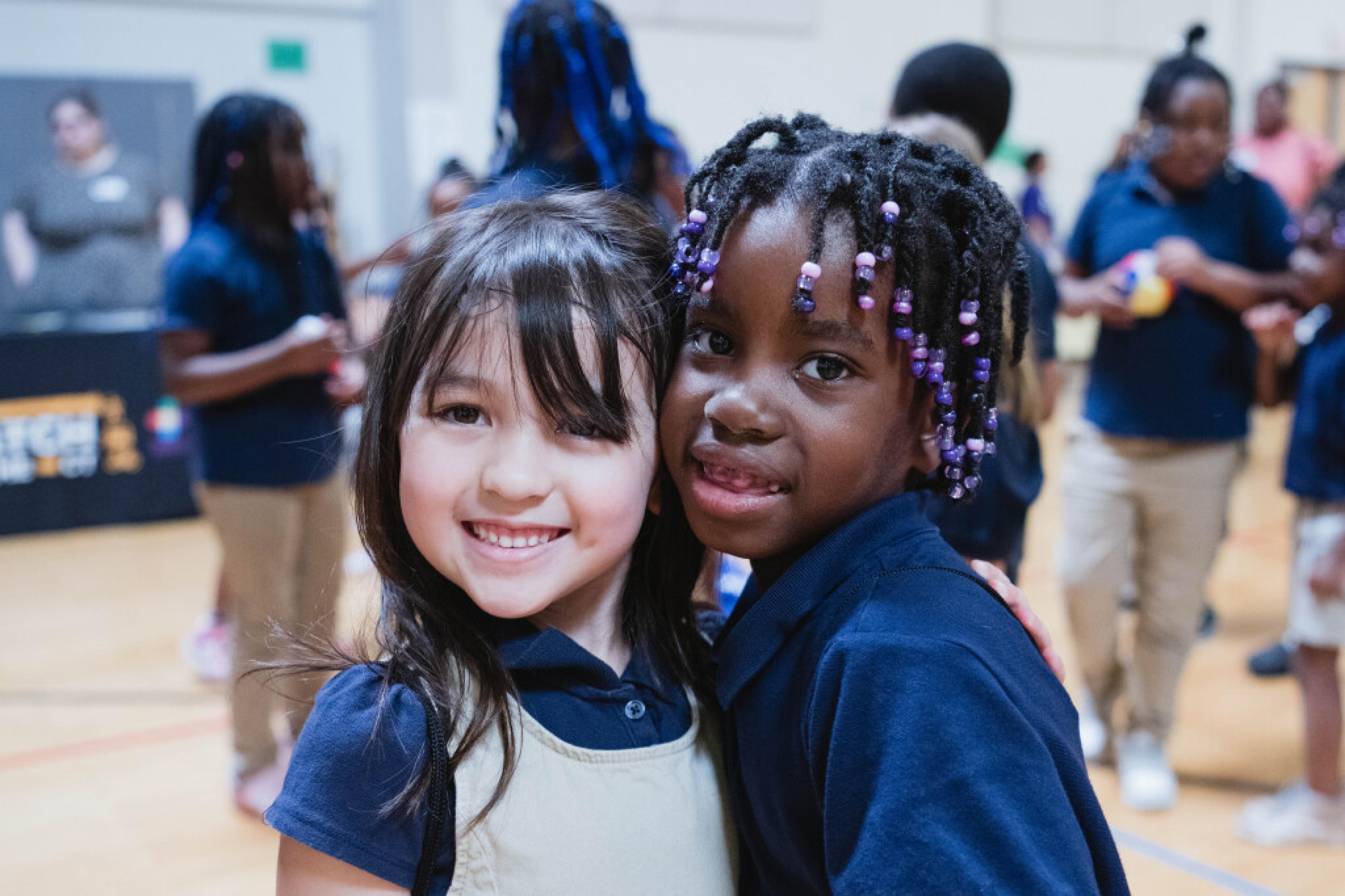 Two school age children pose for a photo in a elementary school gym