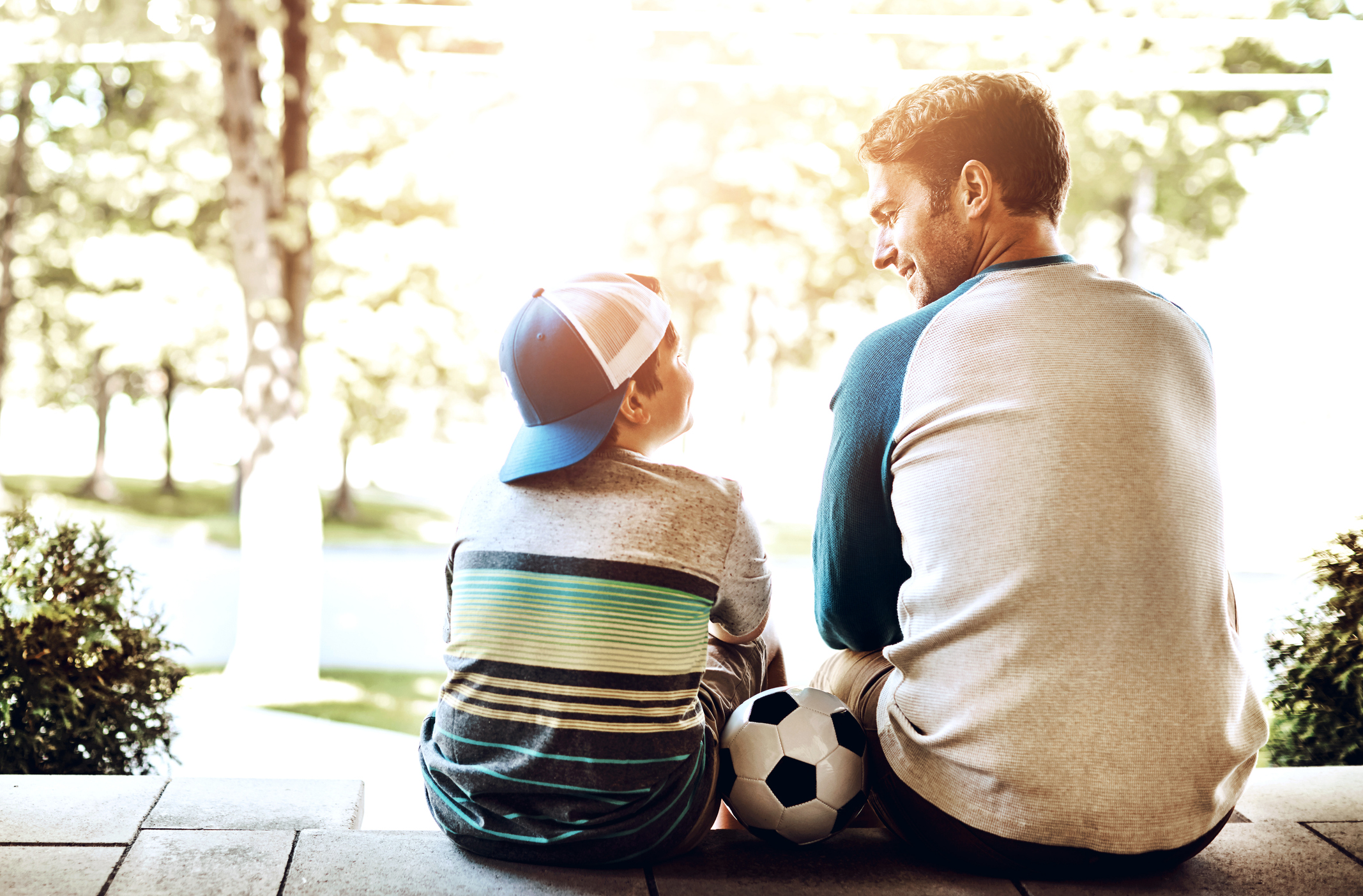 Father and young son, sitting on steps, soccer ball in between them. 