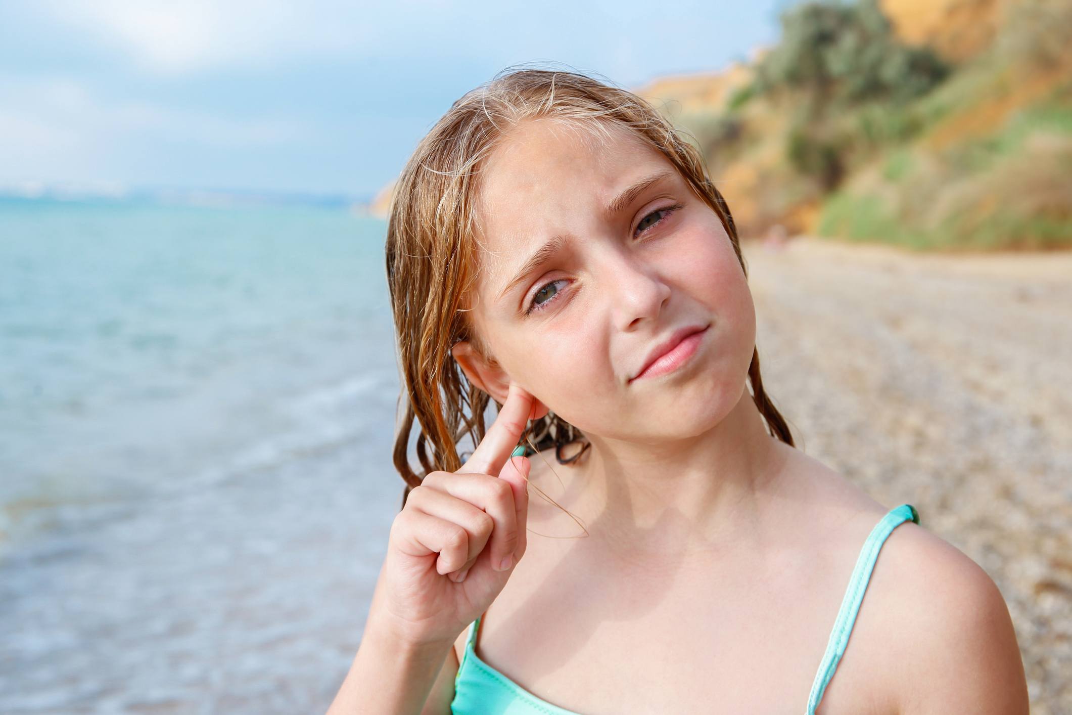 The child got water in his ear while swimming in the sea. The girl cleans her ear from water