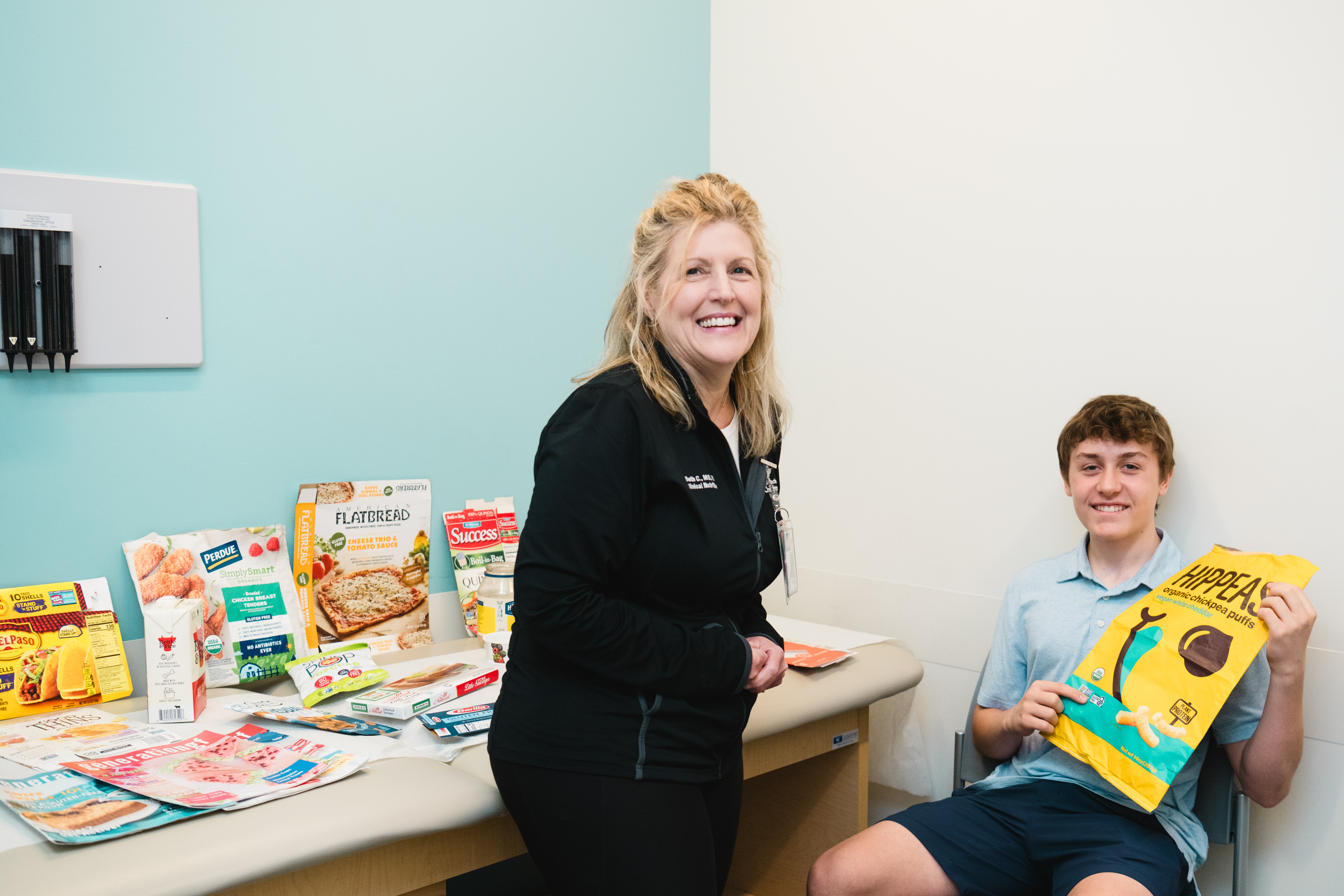 Teenage boy in doctor office holding a bag of Hippeas snacks with female GI clinical nutritionist