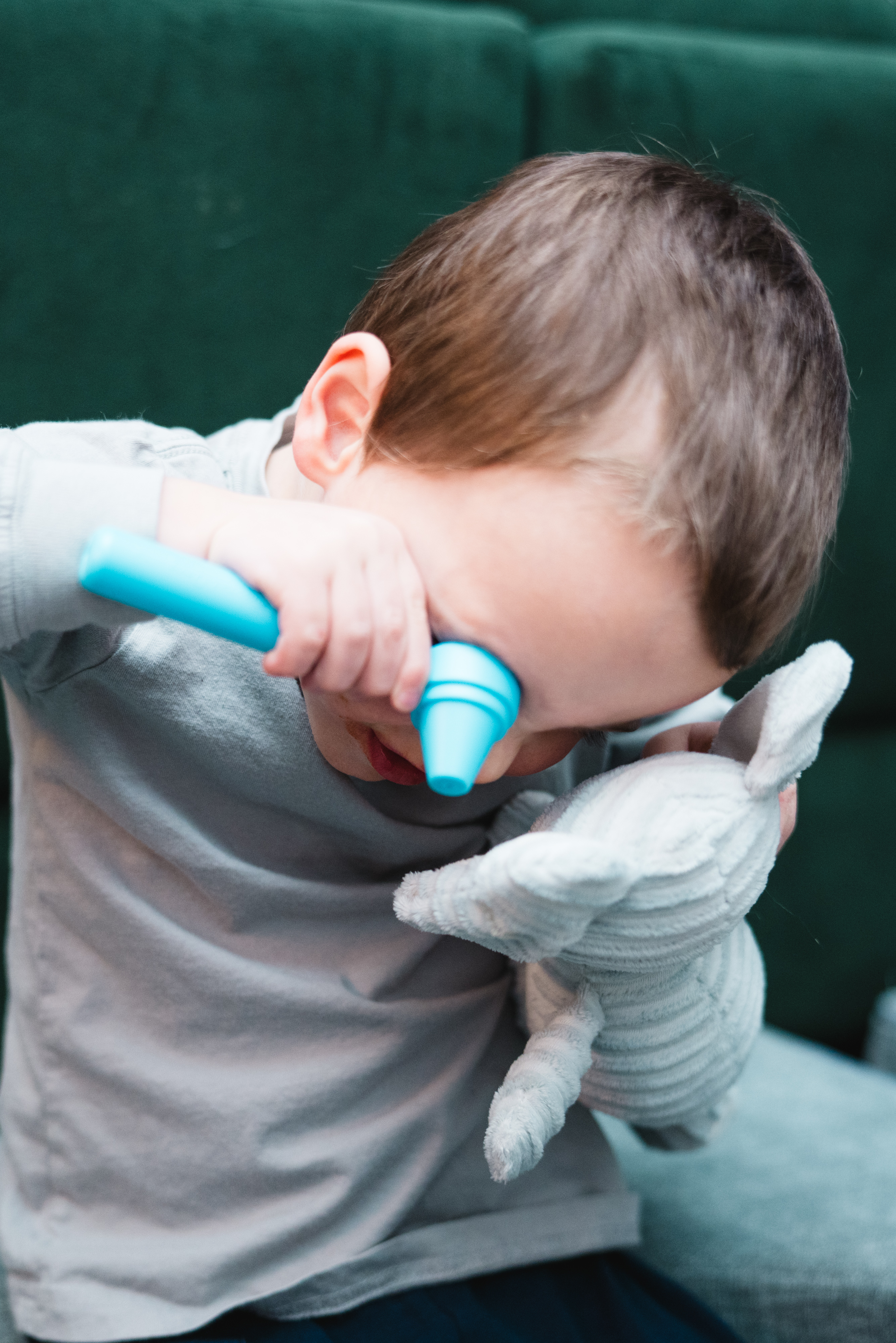 A toddler uses a plastic otoscope to look in a stuffed elephant's ear.
