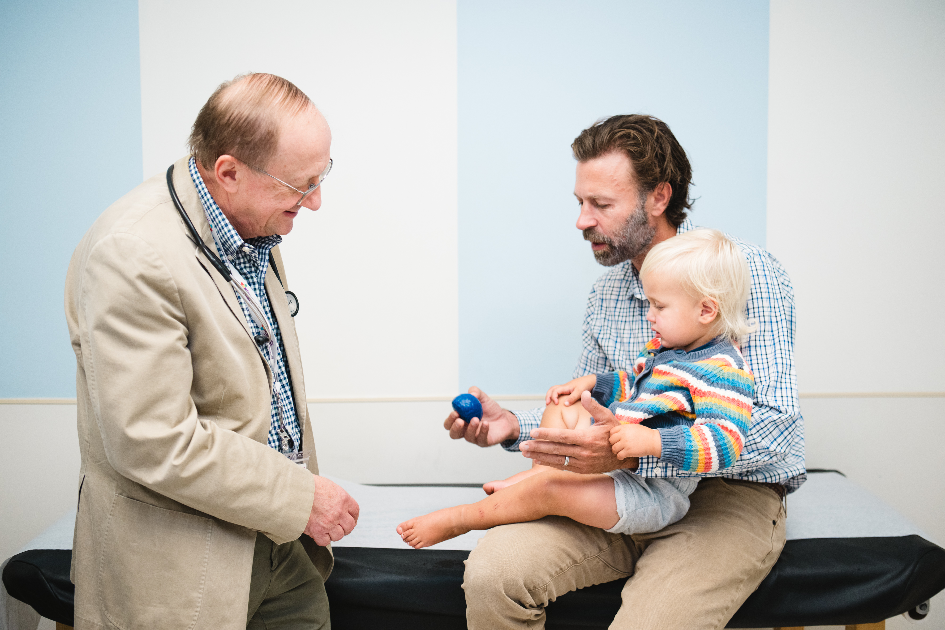 A neurology patient is examined by his doctor while his dad holds him.