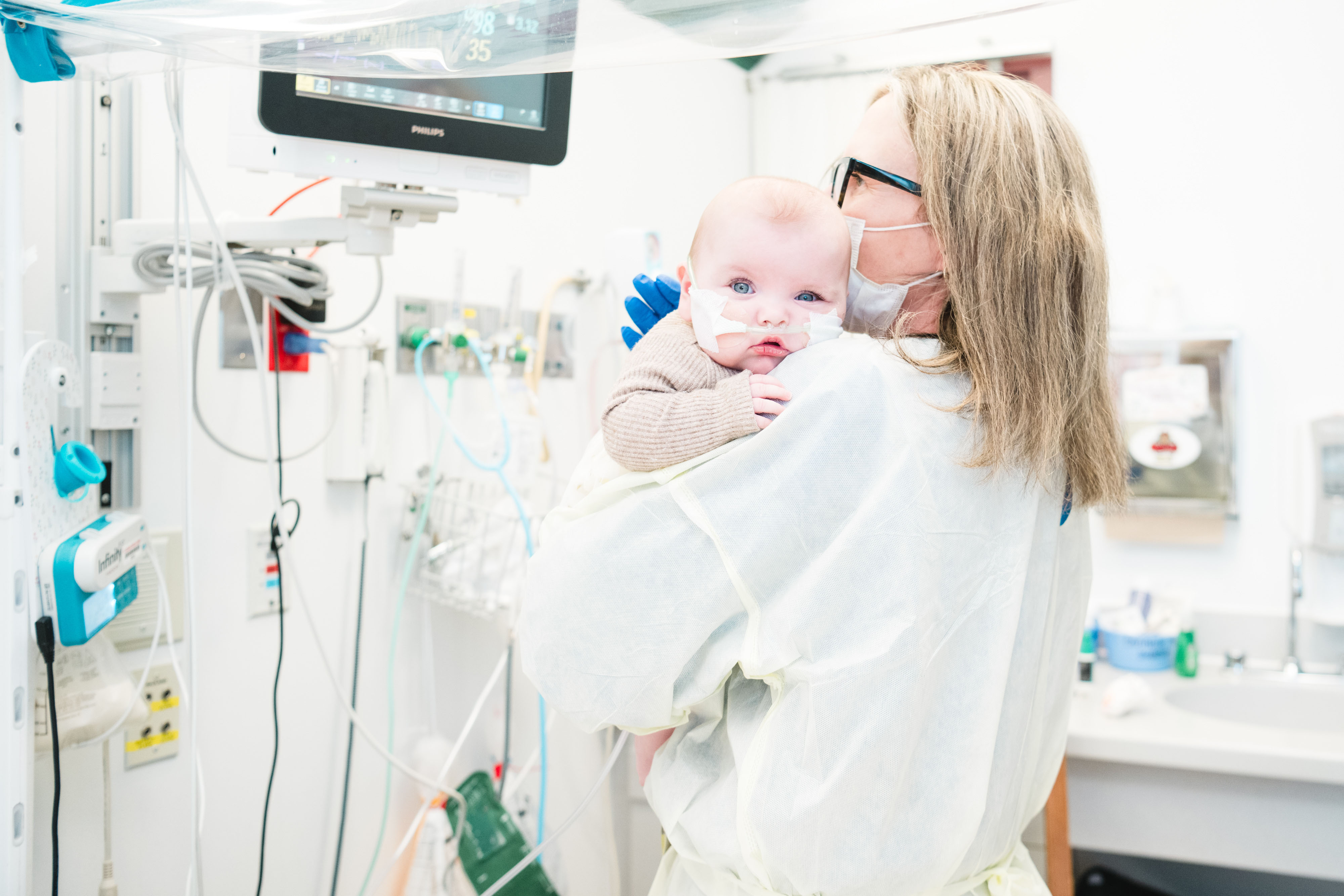 A pain and palliative medicine nurse practitioner holds a baby in a hospital room. A pain and palliative medicine nurse practitioner holds a baby in a hospital room.