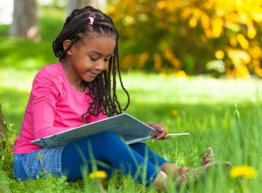 A young girl sits outside and reads a book
