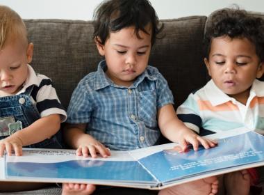 3 toddlers look at a book