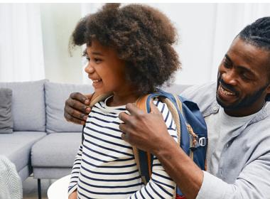 A dad helps his child put their backpack on