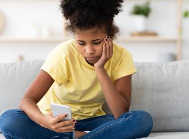 A young girl sits and looks sadly at her phone