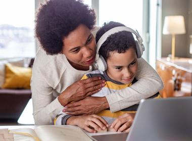 A mother hugs her son while he's on the computer