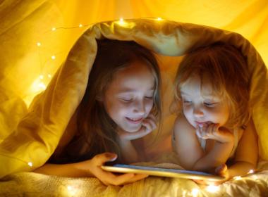 Two young girls hide under a blanket