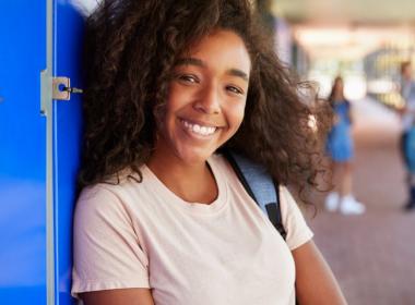 A young girl smiles and leans against her locker