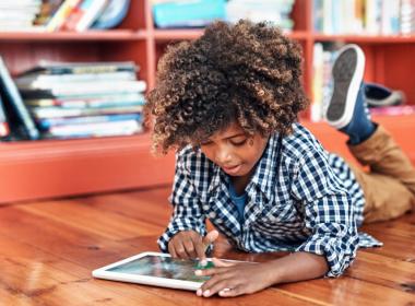 Young boy lies on the ground and plays with a tablet