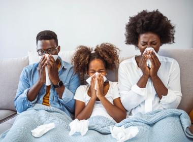 Family of 3, sneezing into tissues on couch.