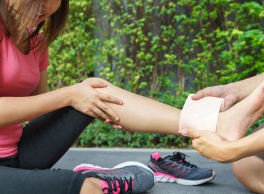 Young adult female athlete stretching leg, icing ankle injury