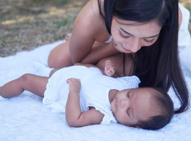 Mom and infant baby outside on blanket, wearing white.