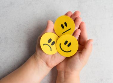 A child holding smiley faces showing different expressions. 