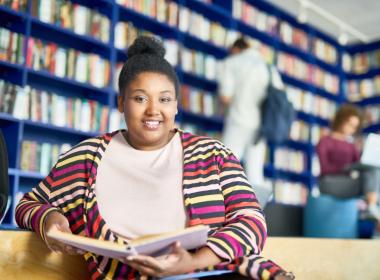 Teenage or young adult woman sitting in library, smiling