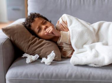 Sick school-aged boy on couch, coughing with tissues