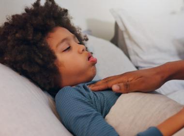 boy coughing in bed, mom's hand on chest