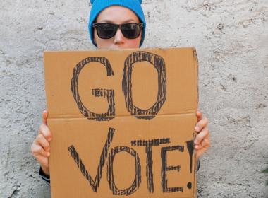 Young woman holding up cardboard sign that says Go Vote!