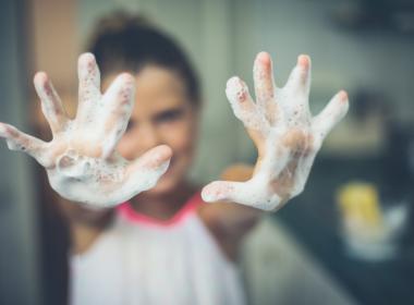 Girl holding up two soapy hands, handwashing facts