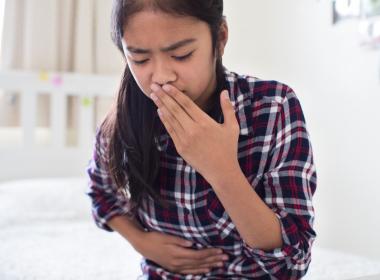 Young girl sitting on bed feeling nauseous