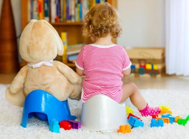 Cute toddler girl sitting on potty next to stuffy on its potty. Backs only