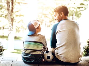 Father and young son, sitting on steps, soccer ball in between them.
