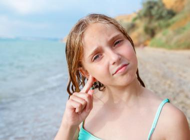 The child got water in his ear while swimming in the sea. The girl cleans her ear from water