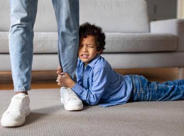 Young boy having tantrum, clinging to parent's leg, laying on floor