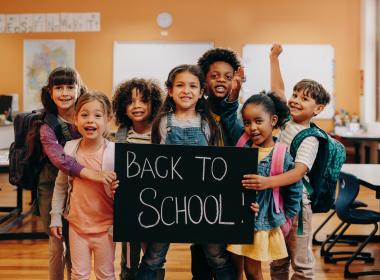 Group of young students in classroom holding "back to school" sign