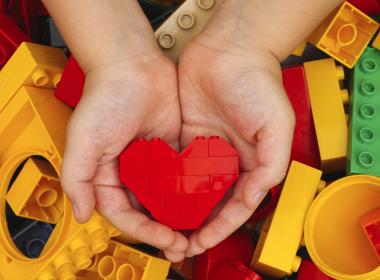 Small child hands holding heart-shaped lego blocks