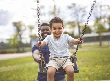 A dad and son playing on the swings together