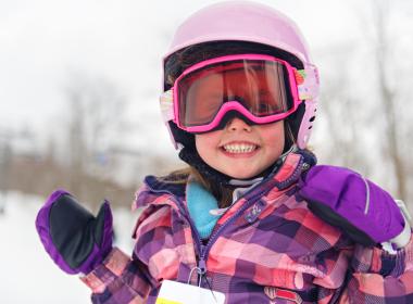 A child playing in the snow wearing ski goggles and ski helmet. 