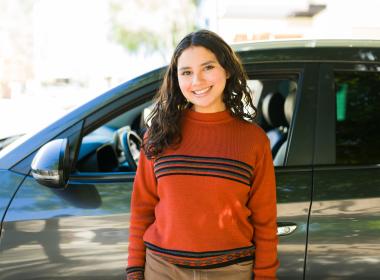 Teen driver standing in front of car