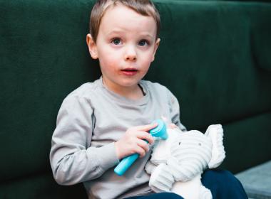 A toddler uses a plastic otoscope to look in a stuffed elephant's ear.