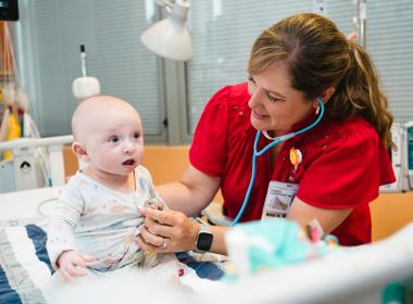 A baby inpatient in the cardiac ICU is examined by his doctor.