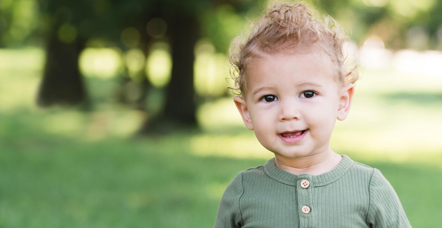 young child smiling in an outside grassy area