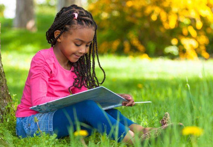 A young girl sits outside and reads a book