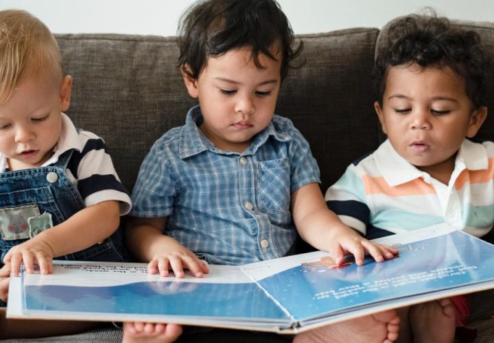 3 toddlers look at a book