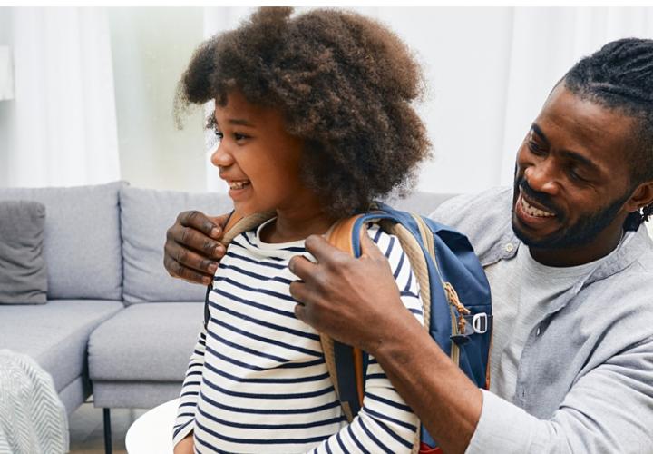 A dad helps his child put their backpack on