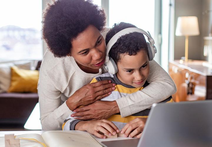 A mother hugs her son while he's on the computer