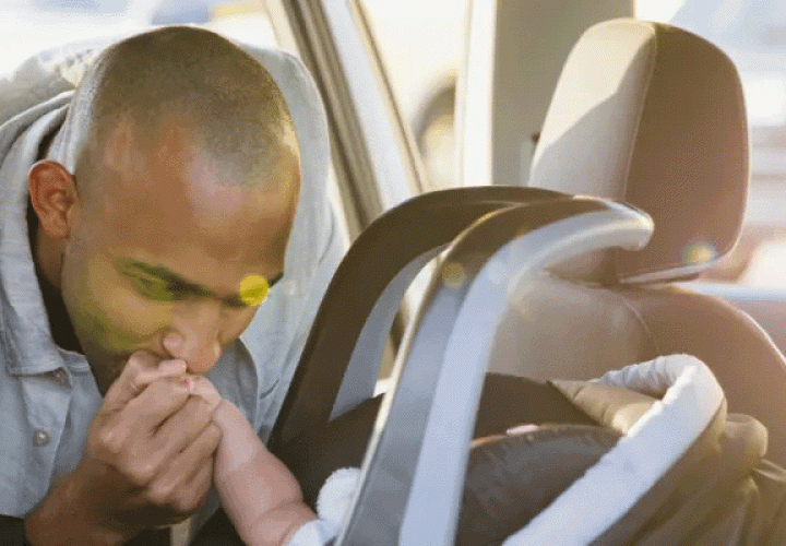 Dad kissing the hand of a child in a car seat
