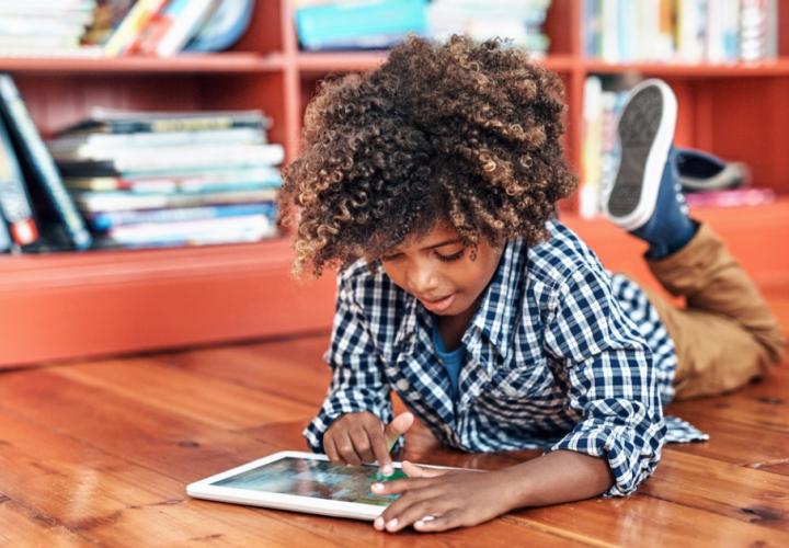 Young boy lies on the ground and plays with a tablet