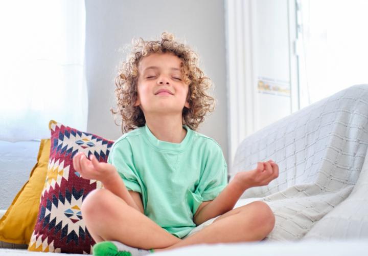 Young boy, practicing meditation on sofa, eyes shut, smiling